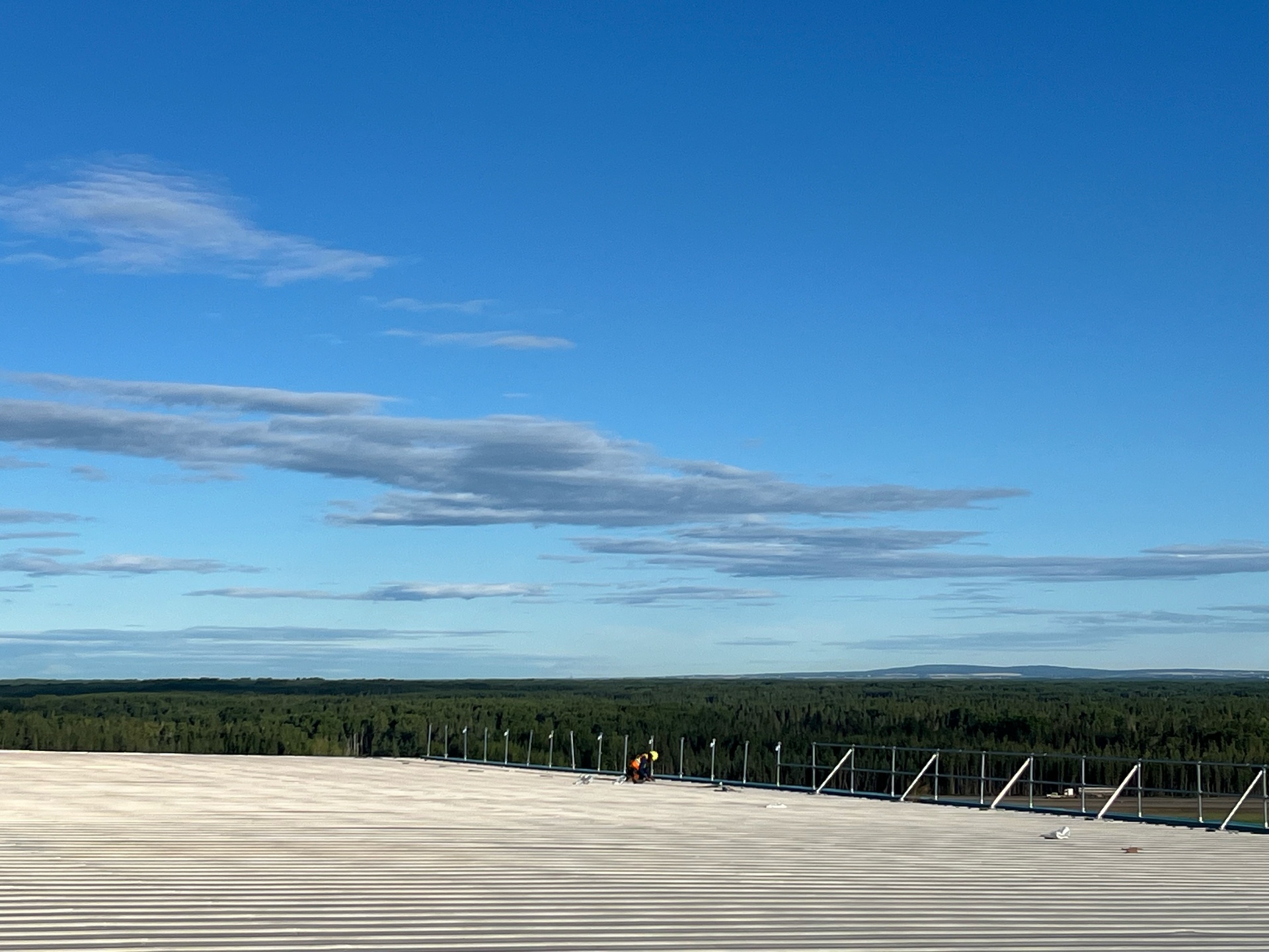 AIM technician working at the edge of a long commercial metal roof with forest and sky beyond