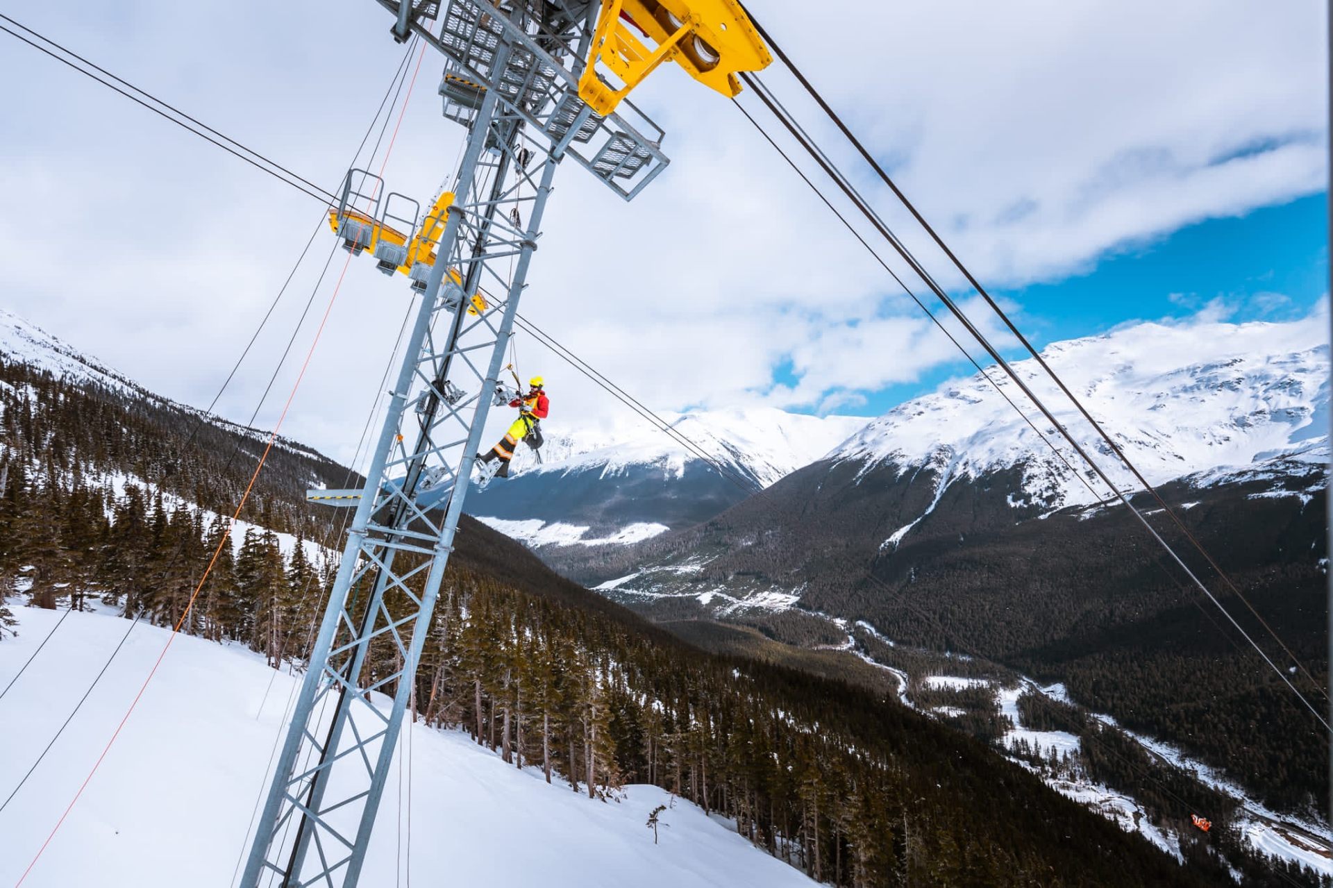Wide mountain panorama with a steel tower and a rope-access technician at work